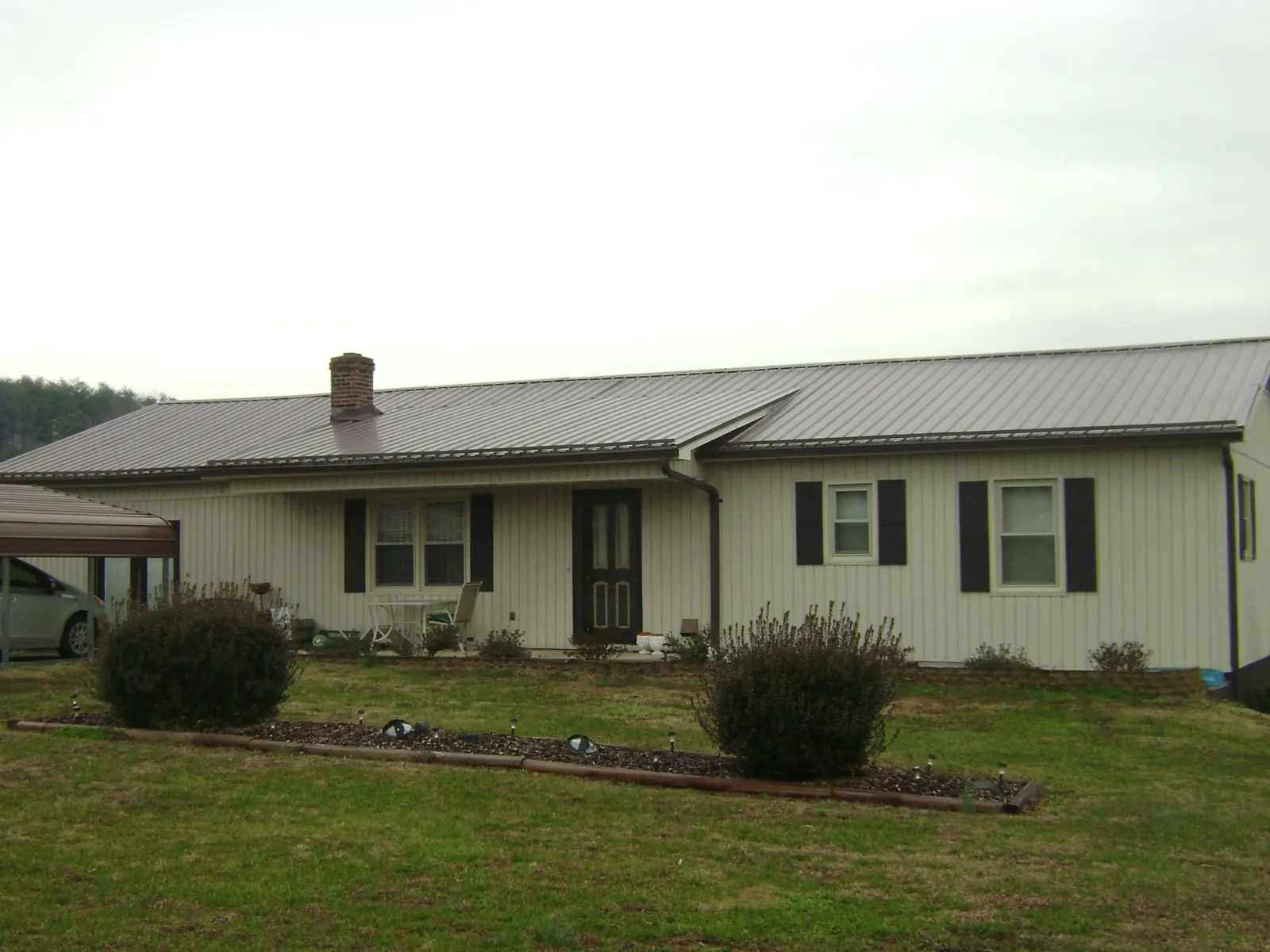 Brown metal roof on a cream sided ranch home with a brick chimney in Butler